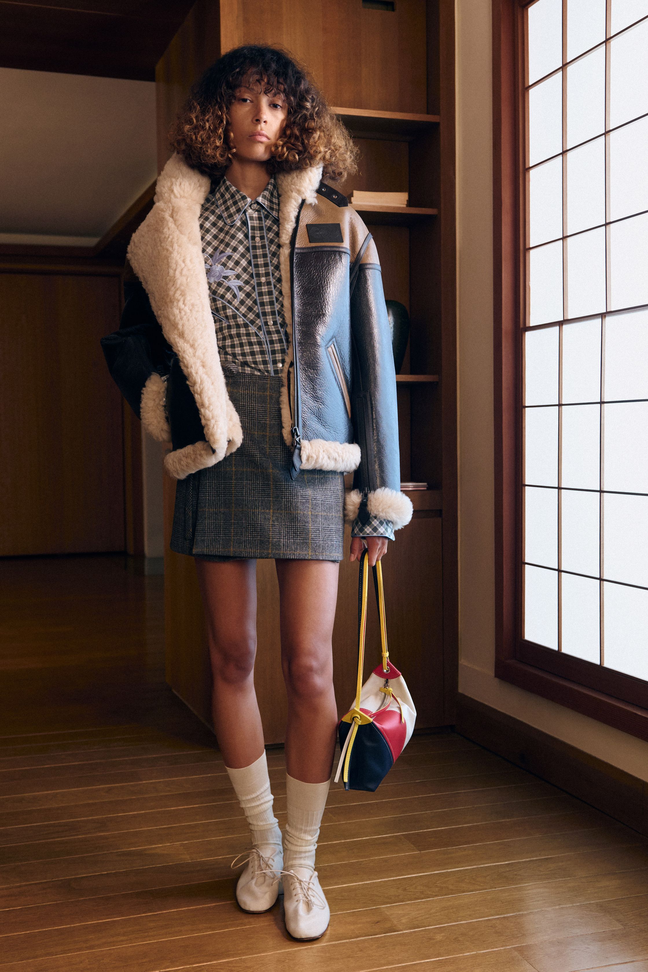 Kenzo 26FW 以“当代旅人”为核心叙事，将日式空间感、巴黎学院派与实穿丹宁重新缝合。剪裁不再强调街头张扬，而是回归比例与层次的节制美学：短外套、羊剪绒飞行夹克、衬衫式连衣廓形在柔光室内场景中显得克制而精准。整体色彩低饱和、结构干净，呈现出一种“被驯化的冒险精神”，让 Kenzo 从符号型街头回到高完成度的现代生活衣橱-顽石频道趋势研究